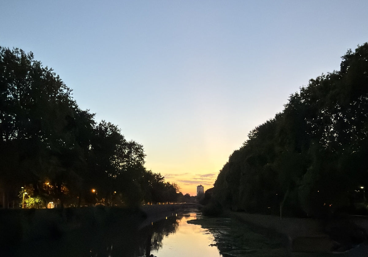 イタリアの街を流れる運河の夕景。両岸に並木が続き、水面に空が映っている